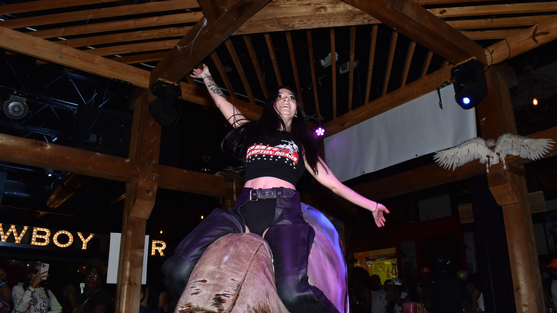 a PBR buckle bunnie wears all black while riding the mechanical bull